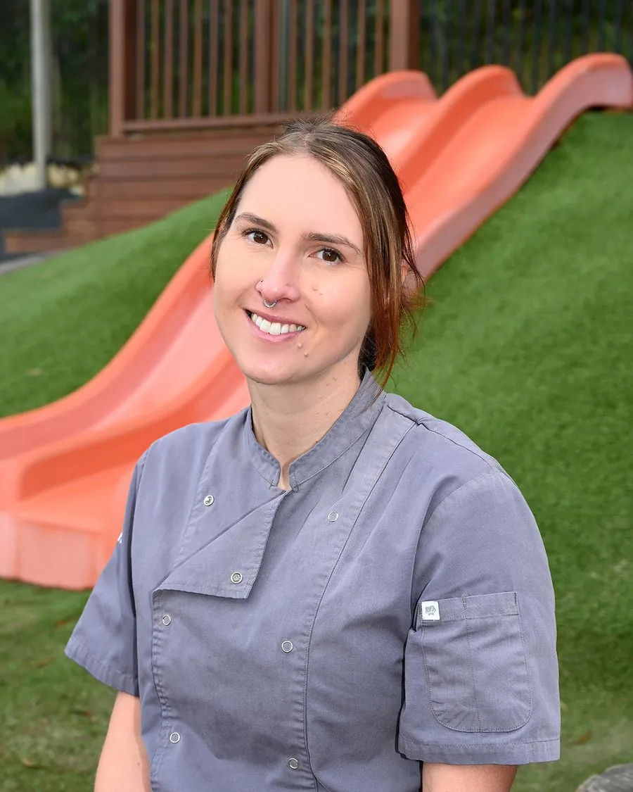 Chef Bec, in her grey chef's jacket, smiling in the playground at The Montessori Farm