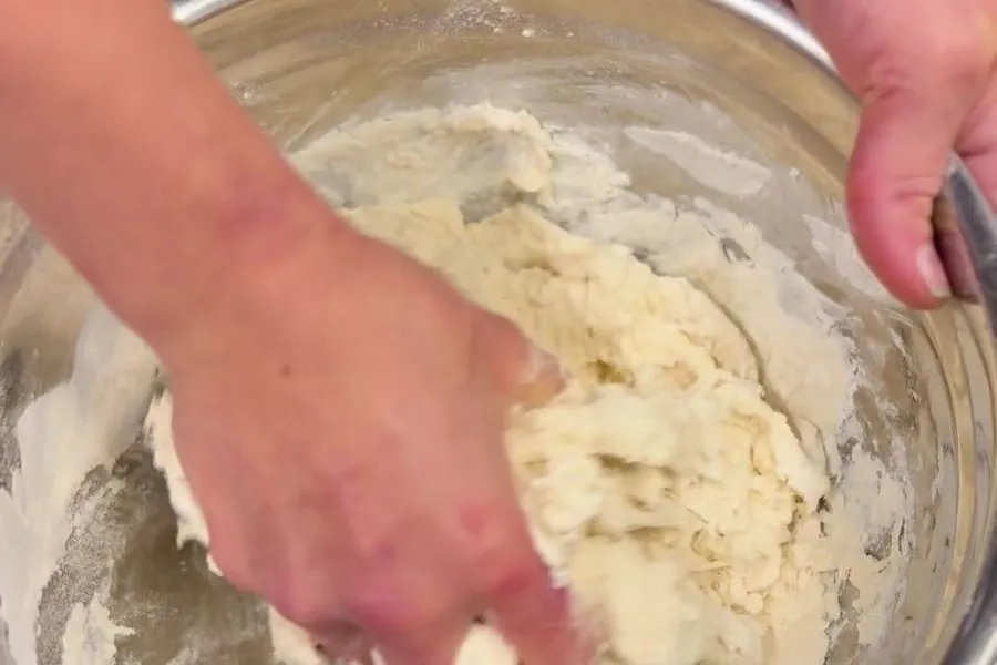 Hands kneading damper dough in a steel mixing bowl