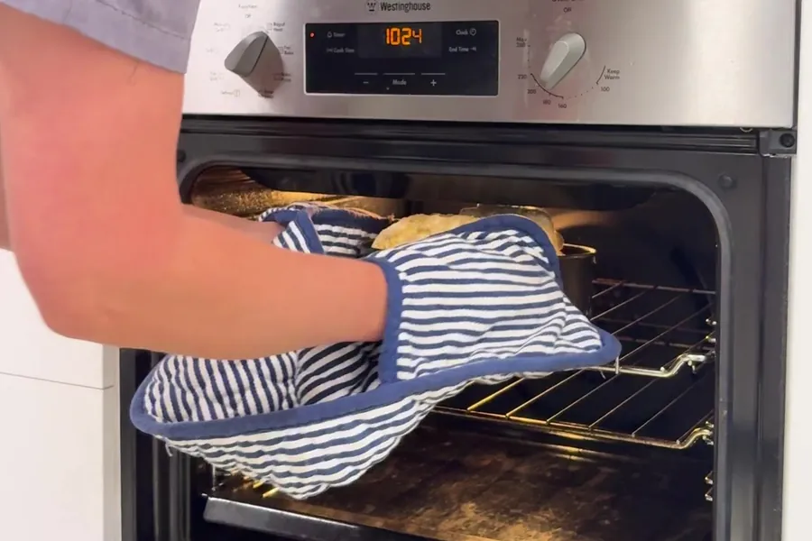 The damper coming out of the oven in striped oven mitts