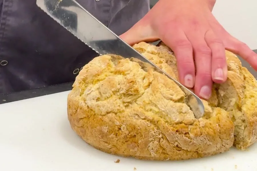 A golden damper loaf being sliced on the kitchen bench