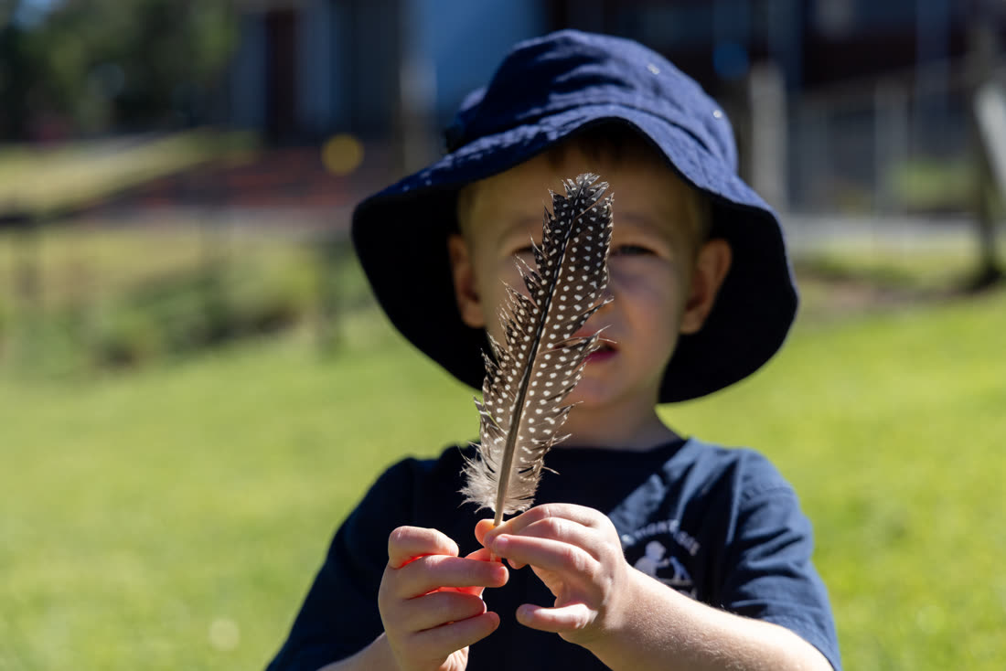 A child holding a feather found on the farm