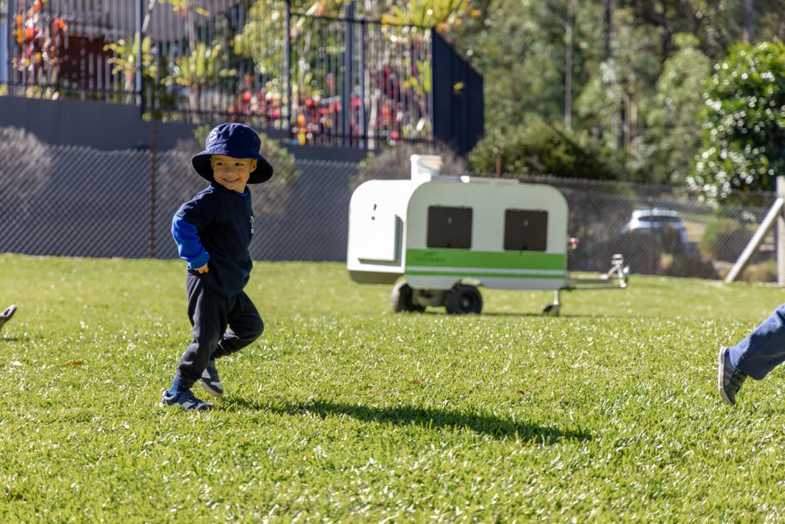 A child running on the grass near the chicken tractor