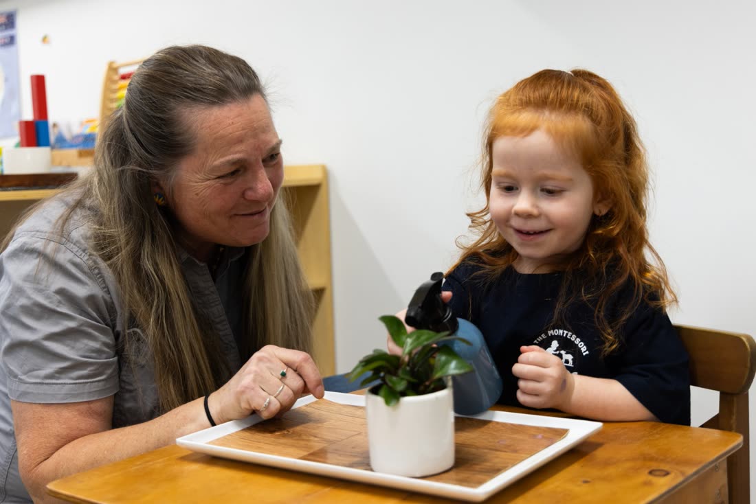 An educator and child tending a plant together